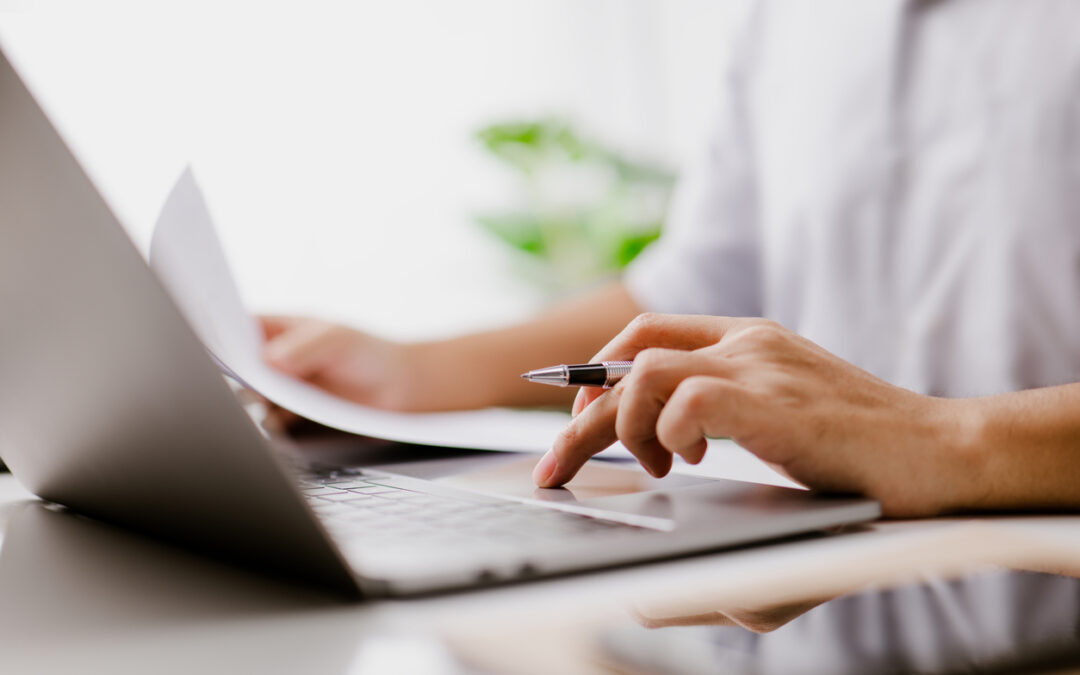 Geschäftsmann sitzt am Laptop und hat Dokumente in der Hand