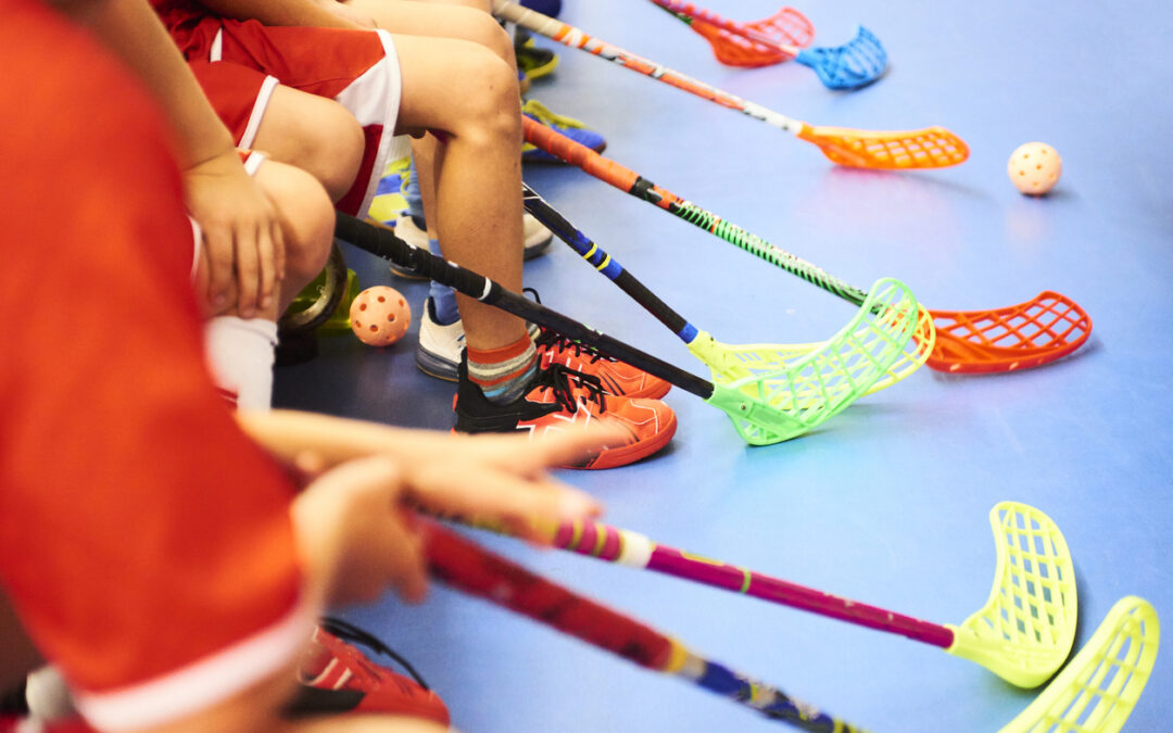 Kinder halten bunte Floorball Schläger in der Hand. Sie sitzen auf einer Bank, man sieht nur Arme und Beine.